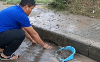 Workers clearing street drainage after heavy rain to prevent flooding by removing debris, mud, and blockages from storm drains for better water flow.