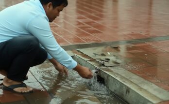 Using a simple tool to unclog a blocked culvert drain during street flooding, restoring water flow and preventing road damage.