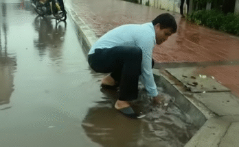Using a simple tool to unclog a blocked culvert drain, restore water flow, and prevent street flooding during heavy rain.